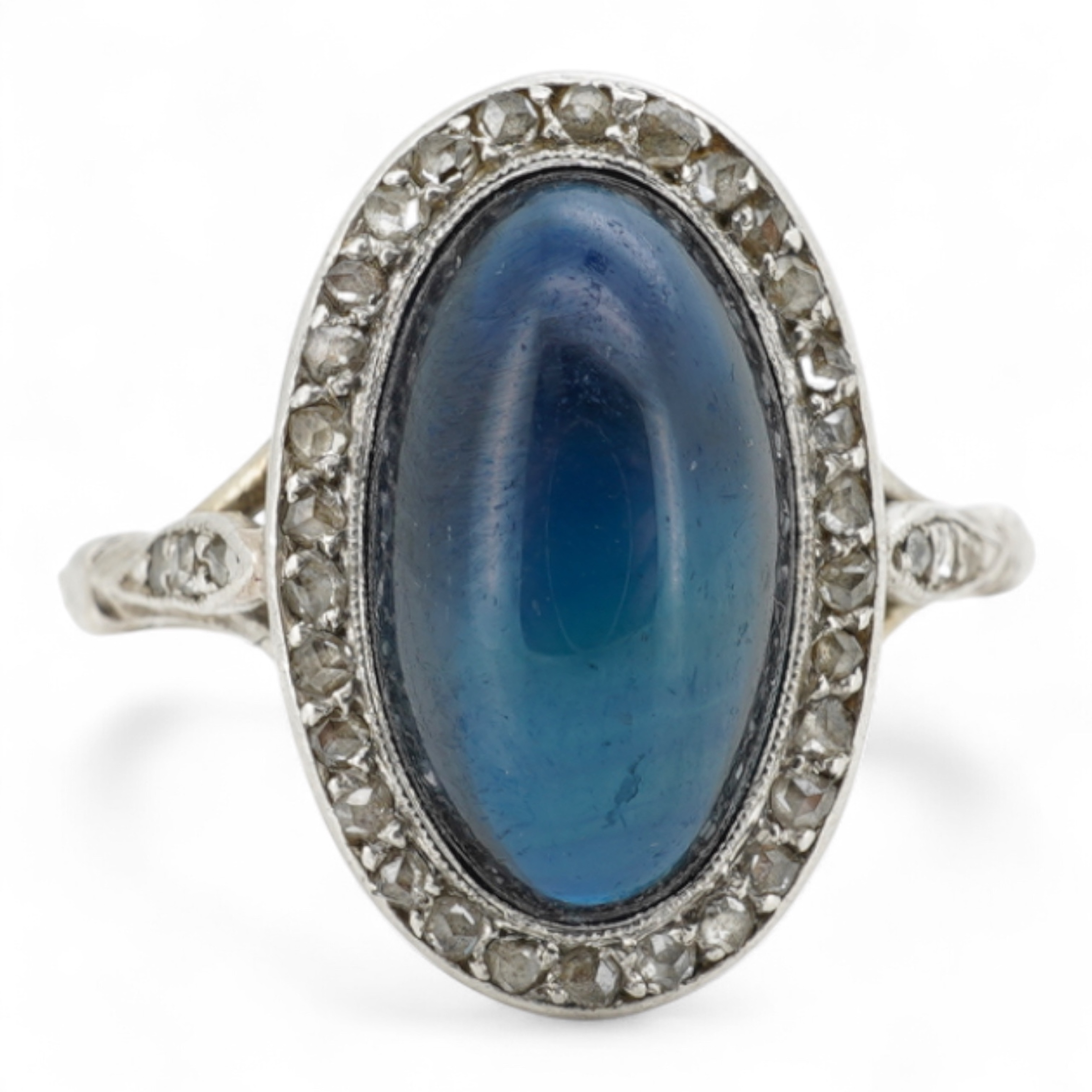 A sapphire and diamond ring, 1920s, set with a cabochon sapphire measuring approximately 2.4 x 6.8 x 4.7mm, within a border of rose-cut diamonds, mounted in platinum, size L1/2